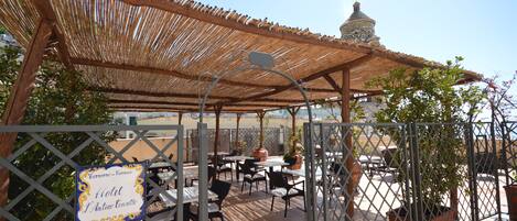 Un área de estar al aire libre con techo, mesas y sillas, un letrero que indica un hotel y una estructura en forma de cúpula al fondo.