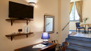 Quarto de hotel com televisão de tela plana, cafeteira, mesa com abajur, cadeira, espelho emoldurado e escada que leva a uma varanda com mesa e cadeiras.