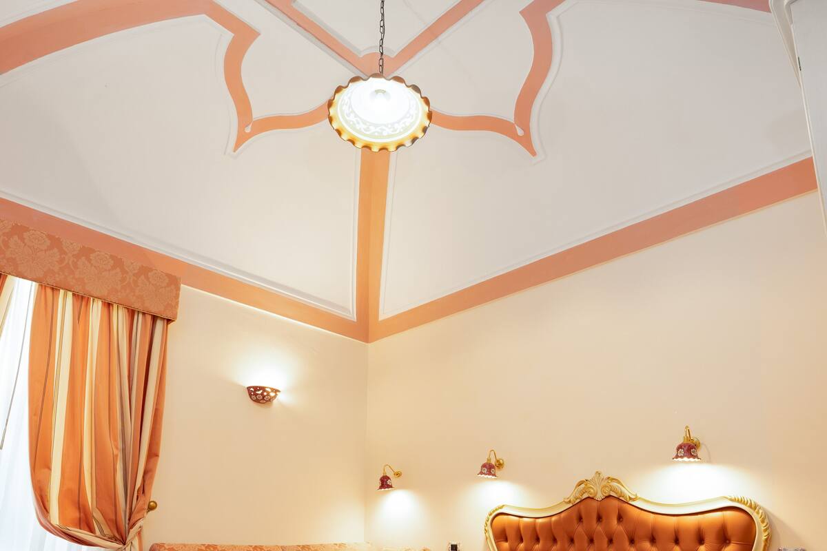 A bedroom with a large bed, a chandelier, and a decorative ceiling.