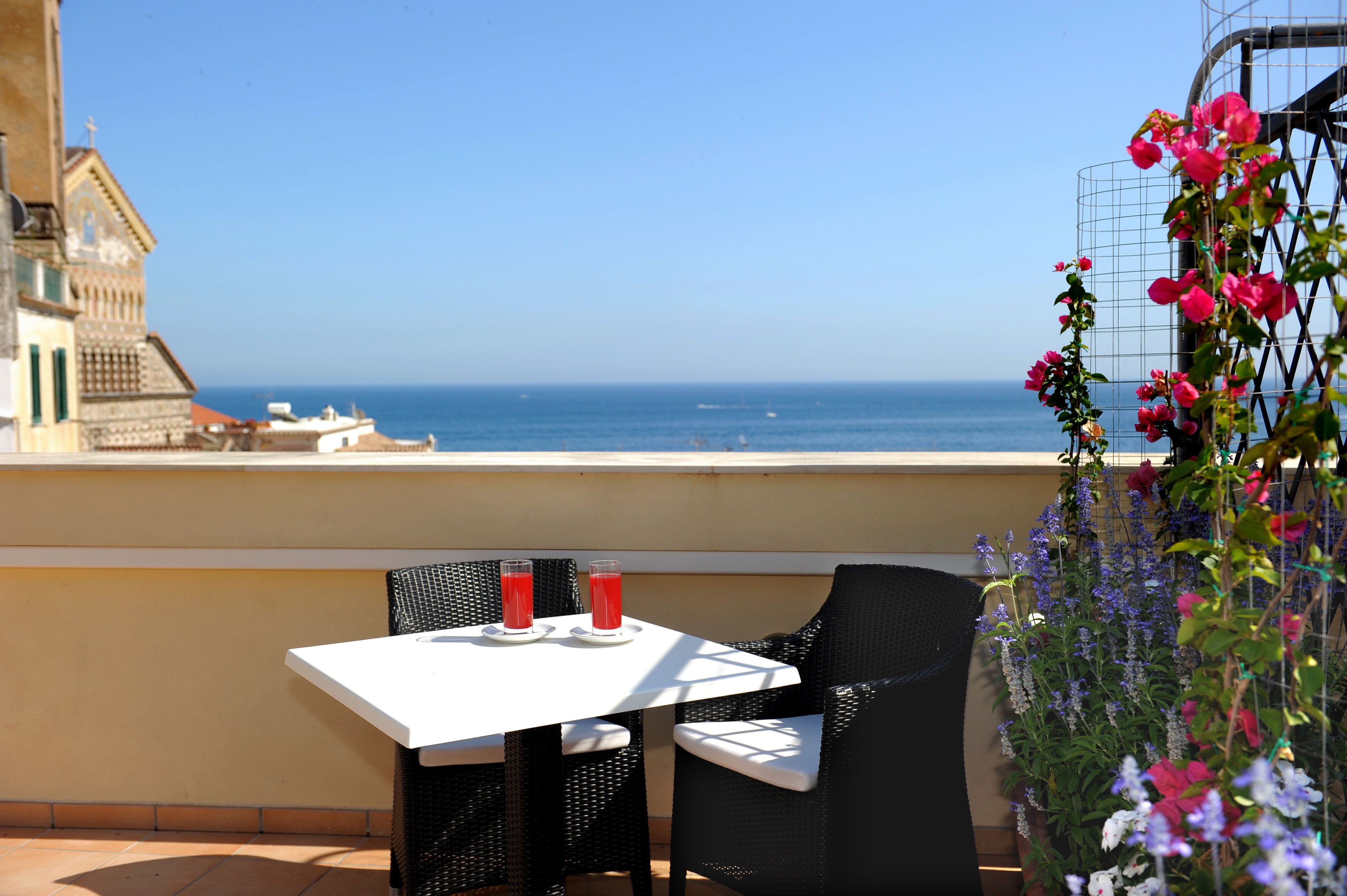 Un balcón con mesa y sillas, vista al mar y un edificio al fondo.