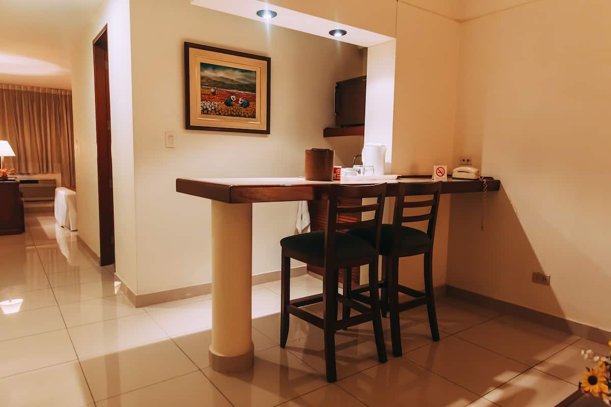 A hotel room with a dining area featuring a wooden table and chairs, a framed picture on the wall, and a telephone.