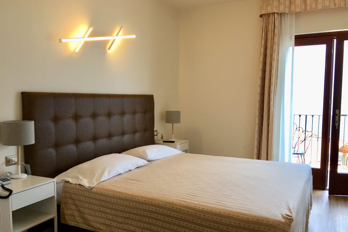 Een hotelkamer met een groot bed, twee nachtkastjes, een modern hoofdeinde en een balkon met een hekwerk.