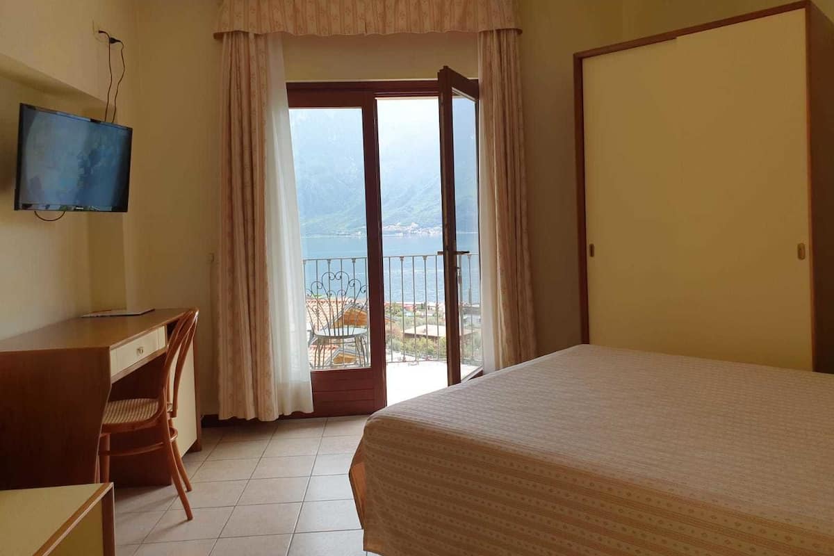 Een hotelkamer met een bed, een bureau, een stoel, een televisie en een balkon met uitzicht op zee.