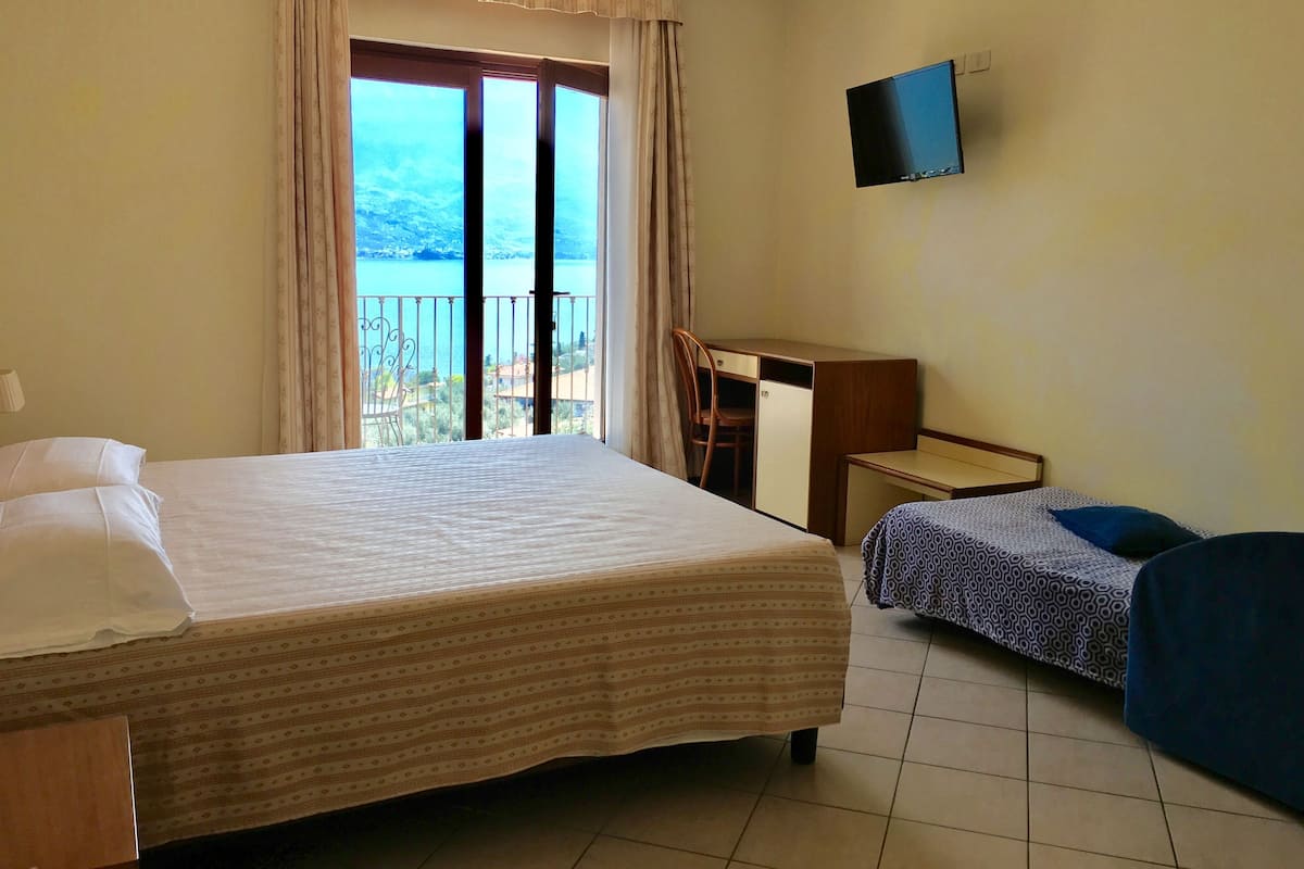Hotelkamer met een groot bed, een bureau, een stoel, een televisie en een balkon met uitzicht op zee.