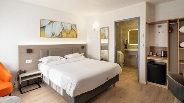 Habitación de hotel con cama, escritorio, silla, armario y baño visible a través de una puerta abierta.