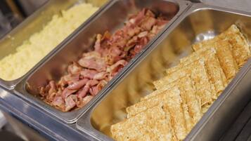 A buffet with various food options including scrambled eggs, bacon, and crepes.