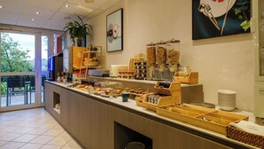 Una barra de desayuno con diferentes alimentos y condimentos, una máquina de café y vistas al exterior.