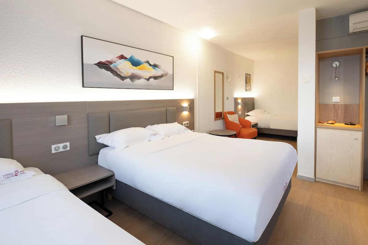 A hotel room with a large bed, bedside tables, a chair, a desk, a wardrobe, and a painting on the wall.