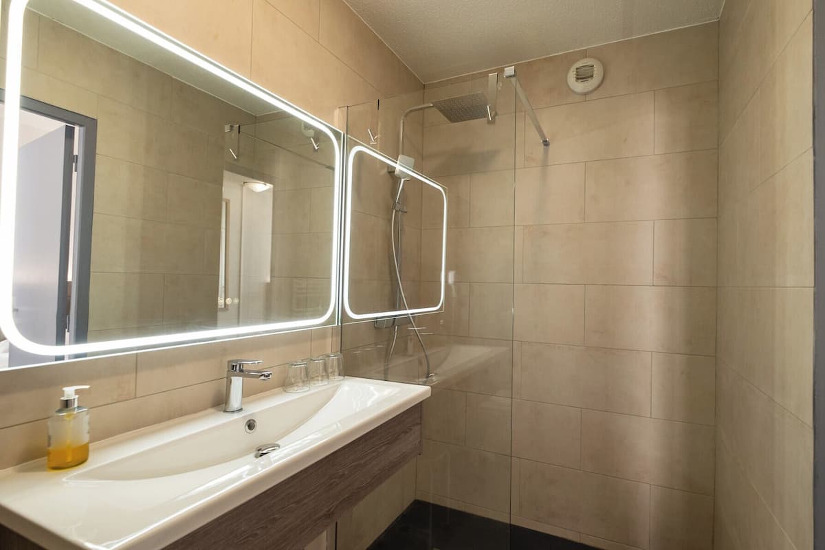 A modern bathroom with a large mirror, two sinks, and a shower.