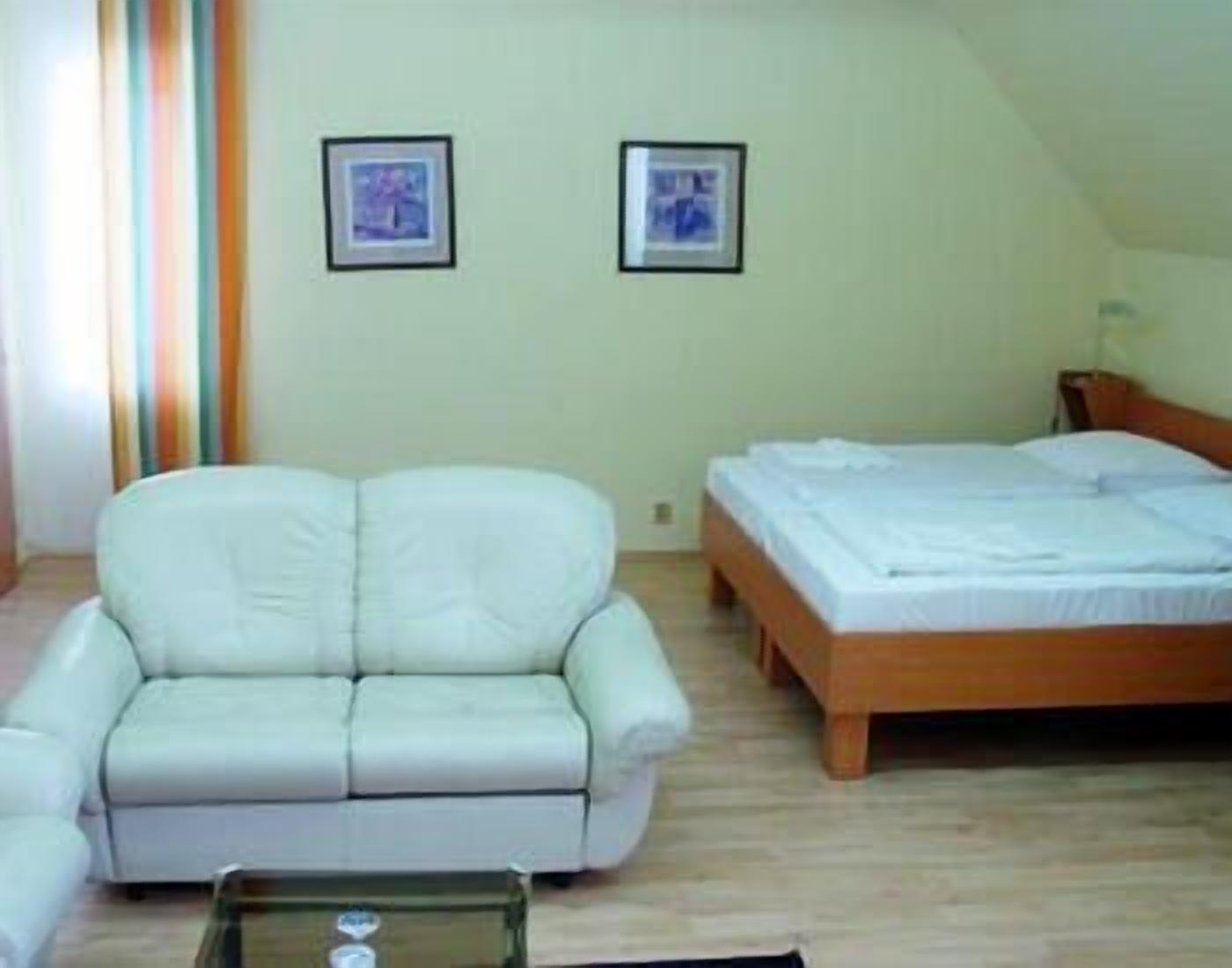 A small, cozy room with a white sofa, a wooden bed, and two framed pictures on the wall.