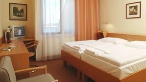 Una camera d'albergo con un letto, una scrivania, una sedia, una televisione e due quadri appesi al muro.