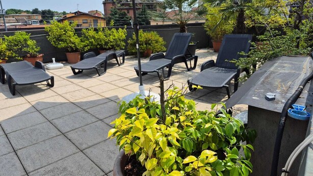 A rooftop terrace with lounge chairs, a large umbrella, and potted plants. - Hotel San Giorgio (Bergamo)