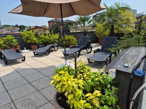 A rooftop terrace with lounge chairs, a large umbrella, and potted plants. - Hotel San Giorgio (Bergamo)