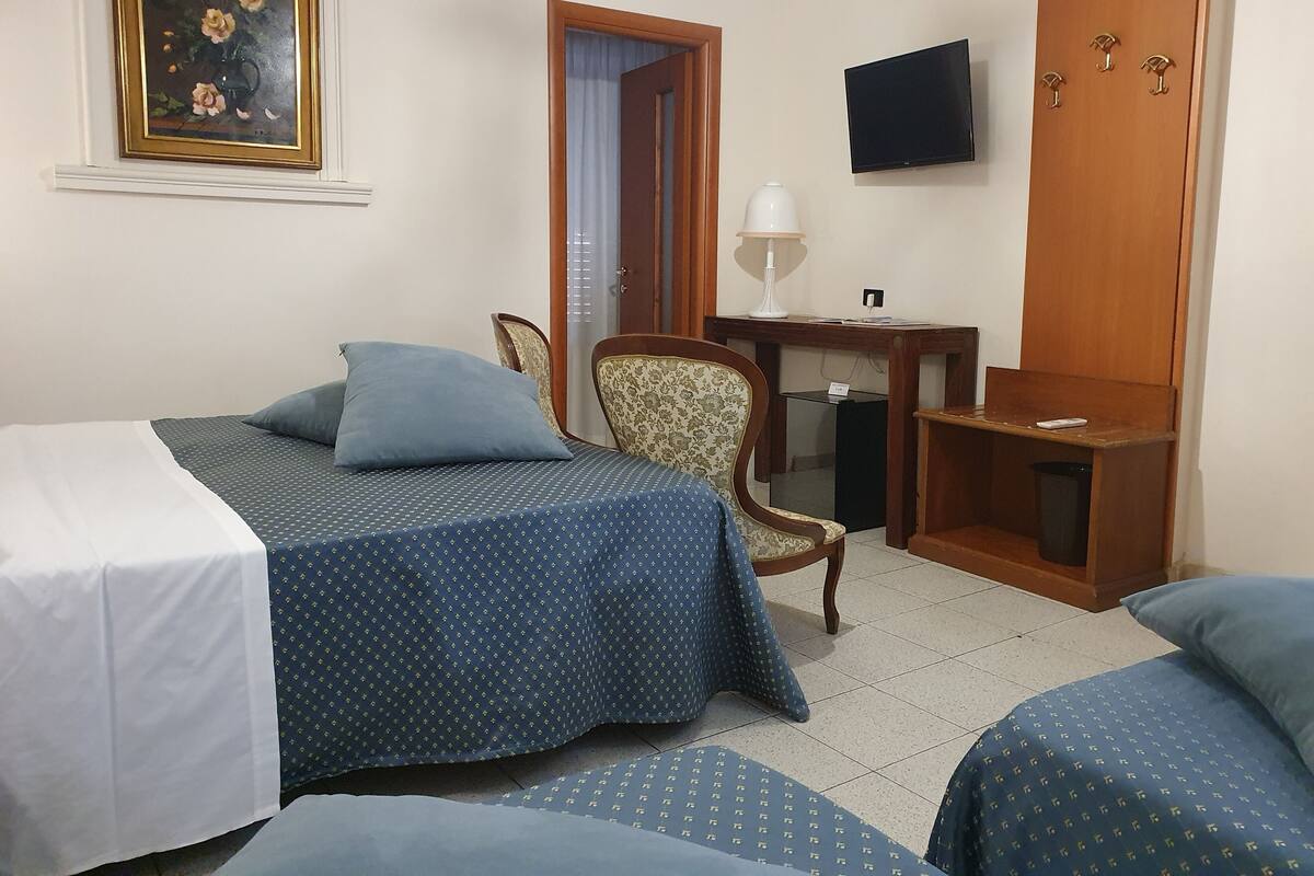 Une chambre d’hôtel avec deux lits, un bureau, une chaise, une télévision et une porte.