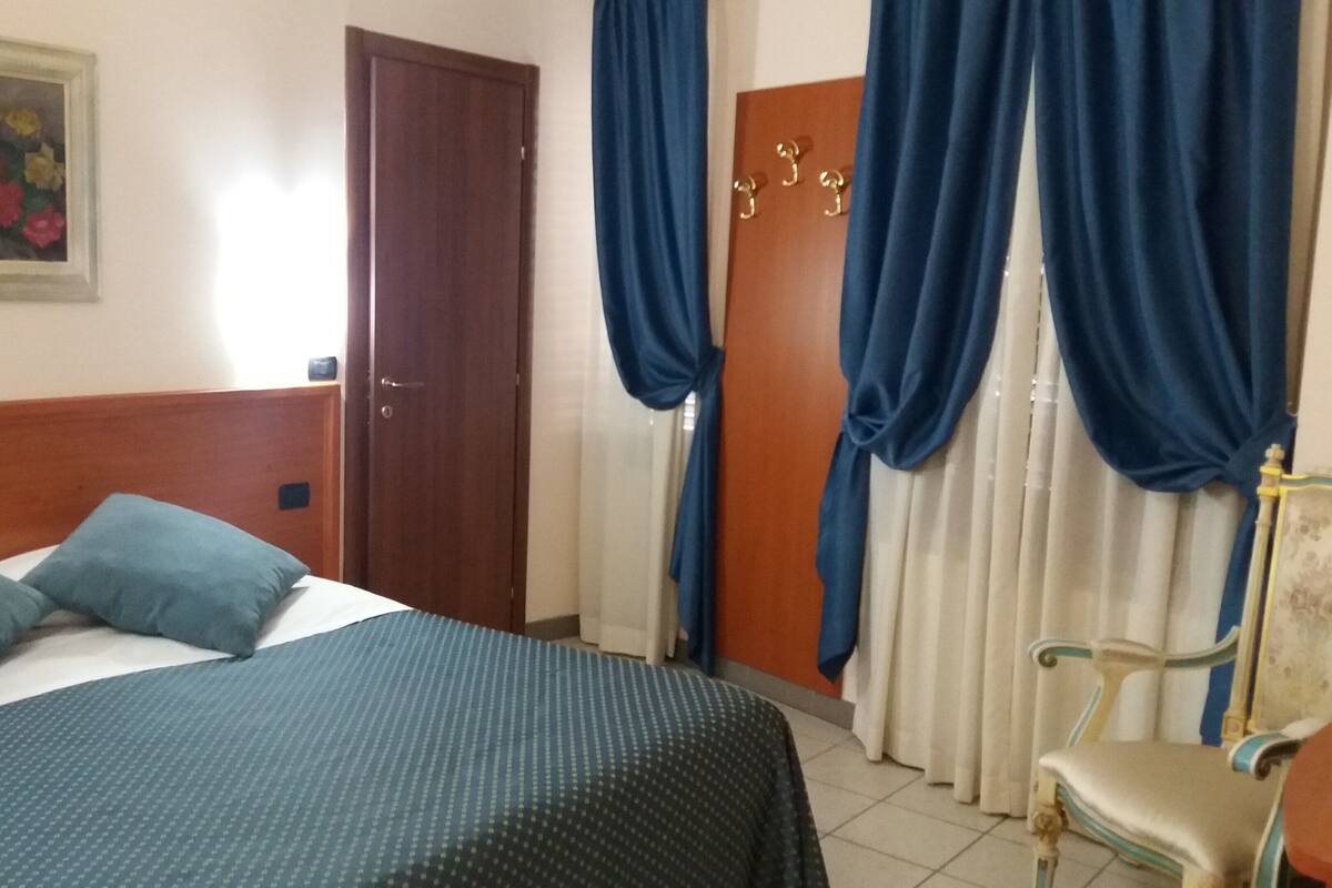 Une chambre d’hôtel avec un lit, des oreillers, une chaise, une porte et des rideaux.