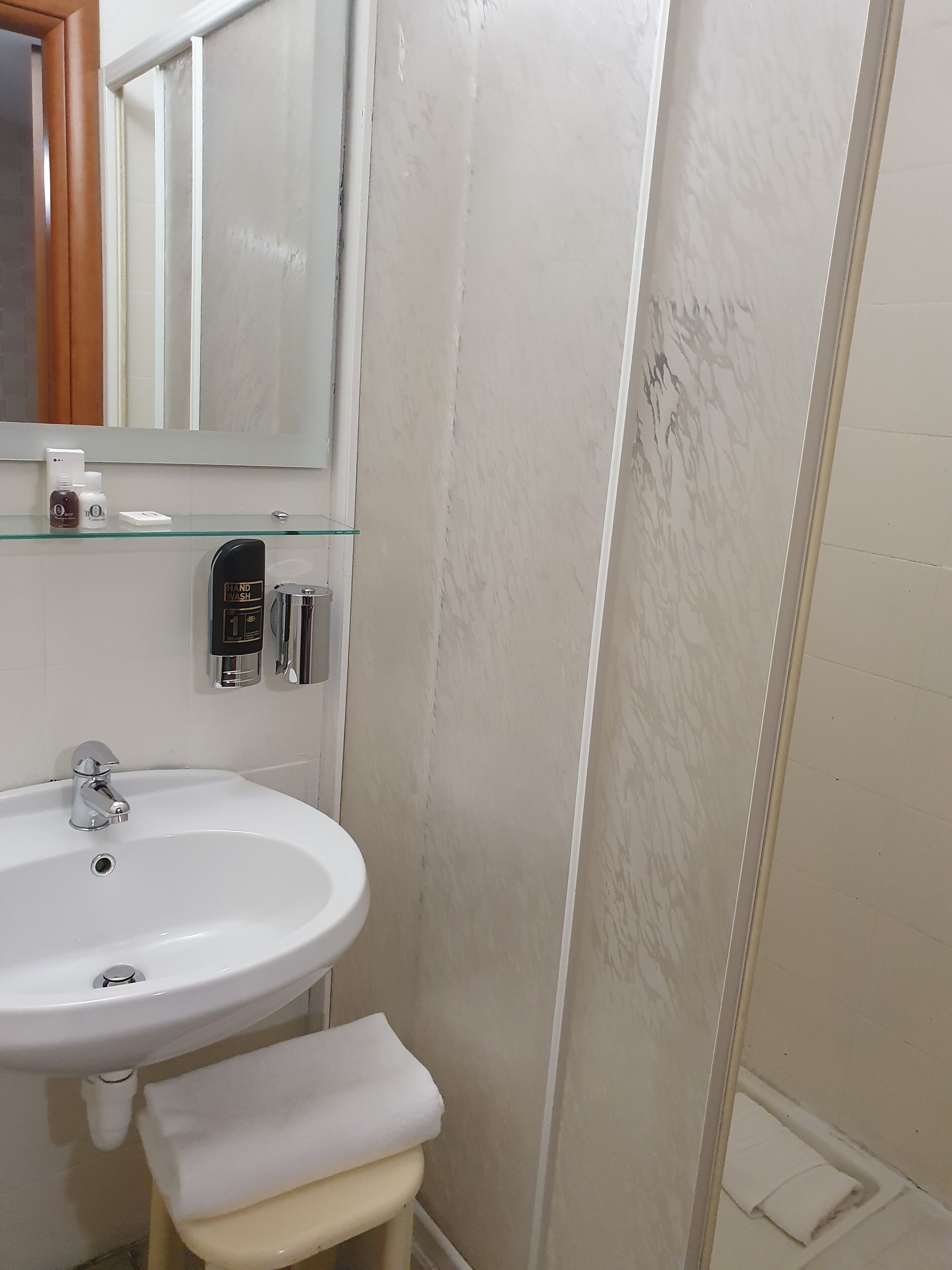 Ein Badezimmer mit einem weißen Waschbecken, einer Glasablage für Toilettenartikel und einer Handwaschstation.