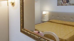 Ein Hotelzimmer mit Bett, Nachttisch, Lampe, Spiegel und einem Bild an der Wand.