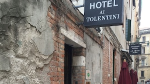 Ein Hotel namens "HOTEL AI TOLENTINI" mit einem Schild über dem Eingang, einer Ziegel-Fassade und Außenplätzen mit Tischen und Stühlen.