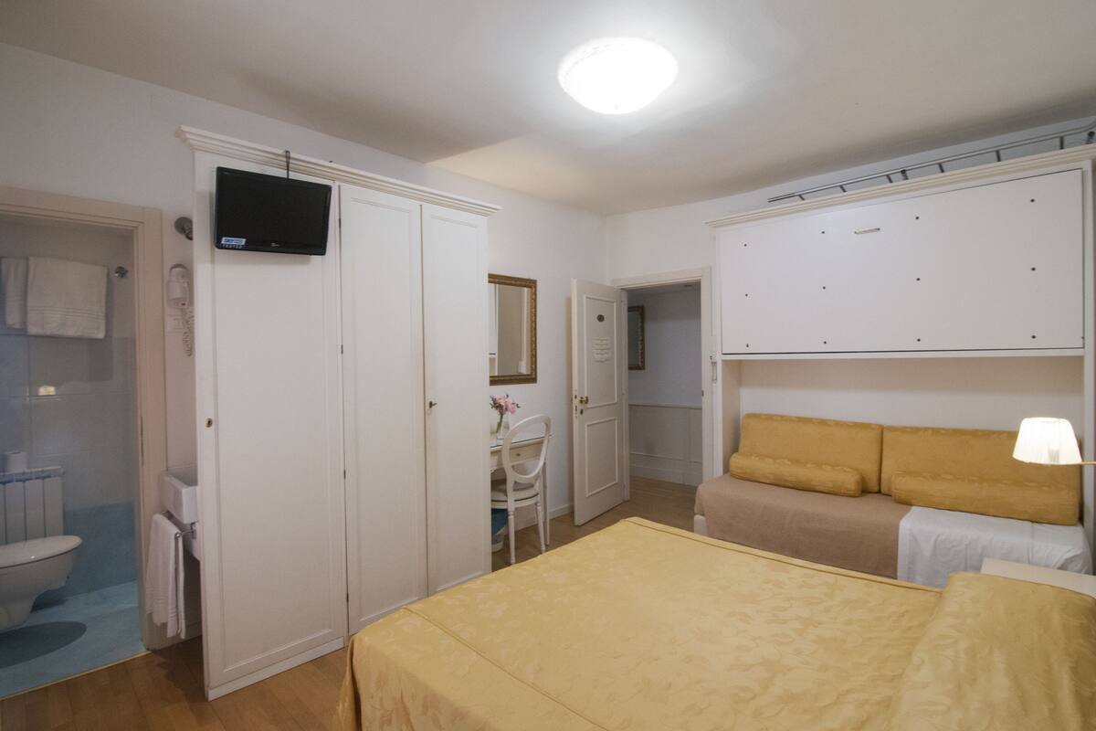 A hotel room with a bed, a desk with a chair, a television, and a wardrobe.