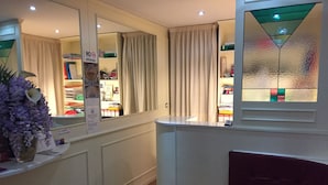 Ein Hotelzimmer mit Holzboden, einem kleinen Tisch mit Blumenmuster-Tischdecke, einem großen Spiegel und einem Fenster mit einem Buntglasdekor.