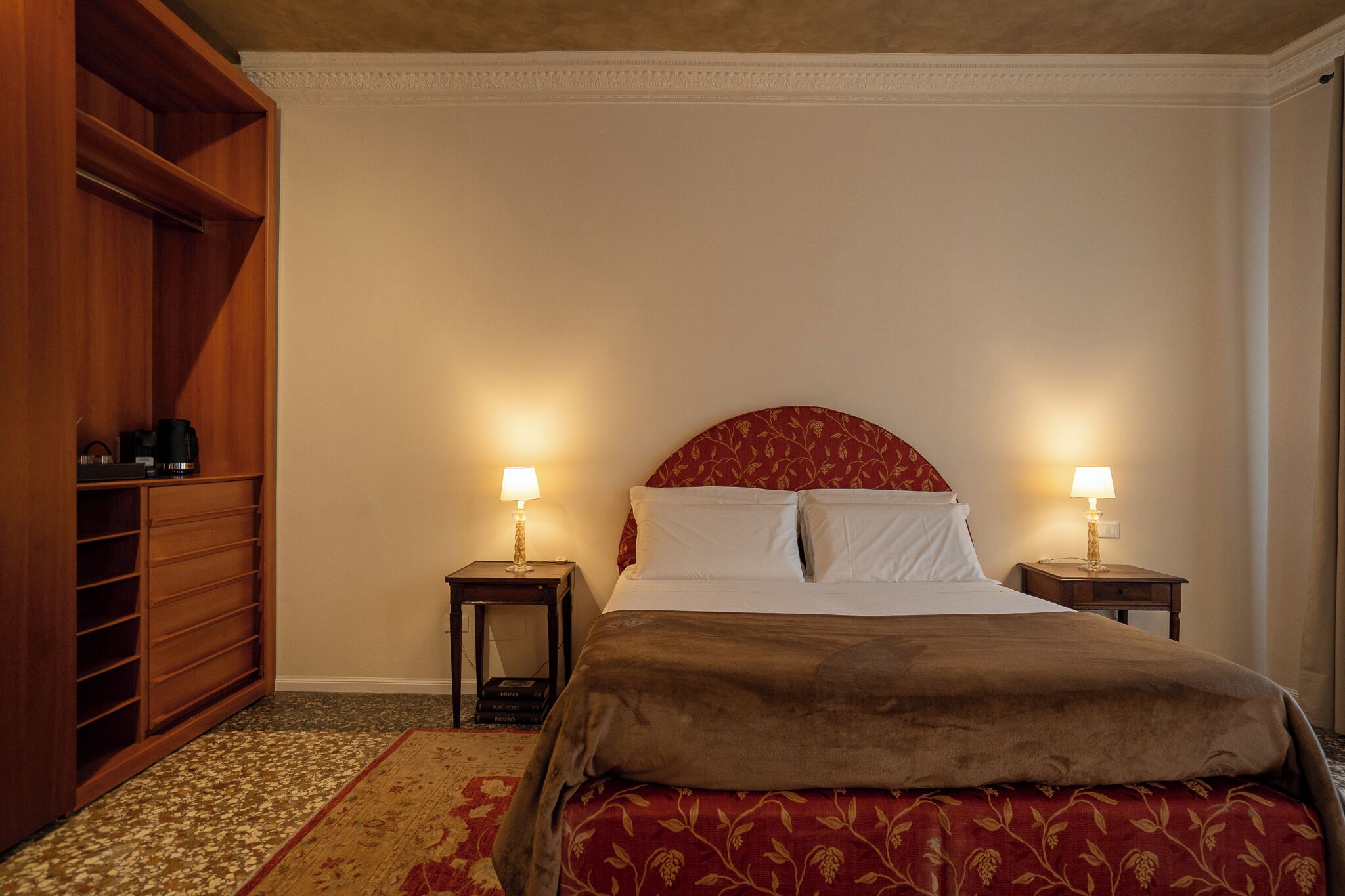 Ein ordentlich eingerichtetes Schlafzimmer mit einem großen Bett, zwei Nachttischen mit Lampen, einem Holzschrank und einem gemusterten Teppich.