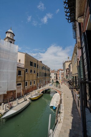 A narrow canal with boats docked on the right, flanked by historic buildings with a bridge in the background. - Ca'Turelli Dimora Storica (Venice)