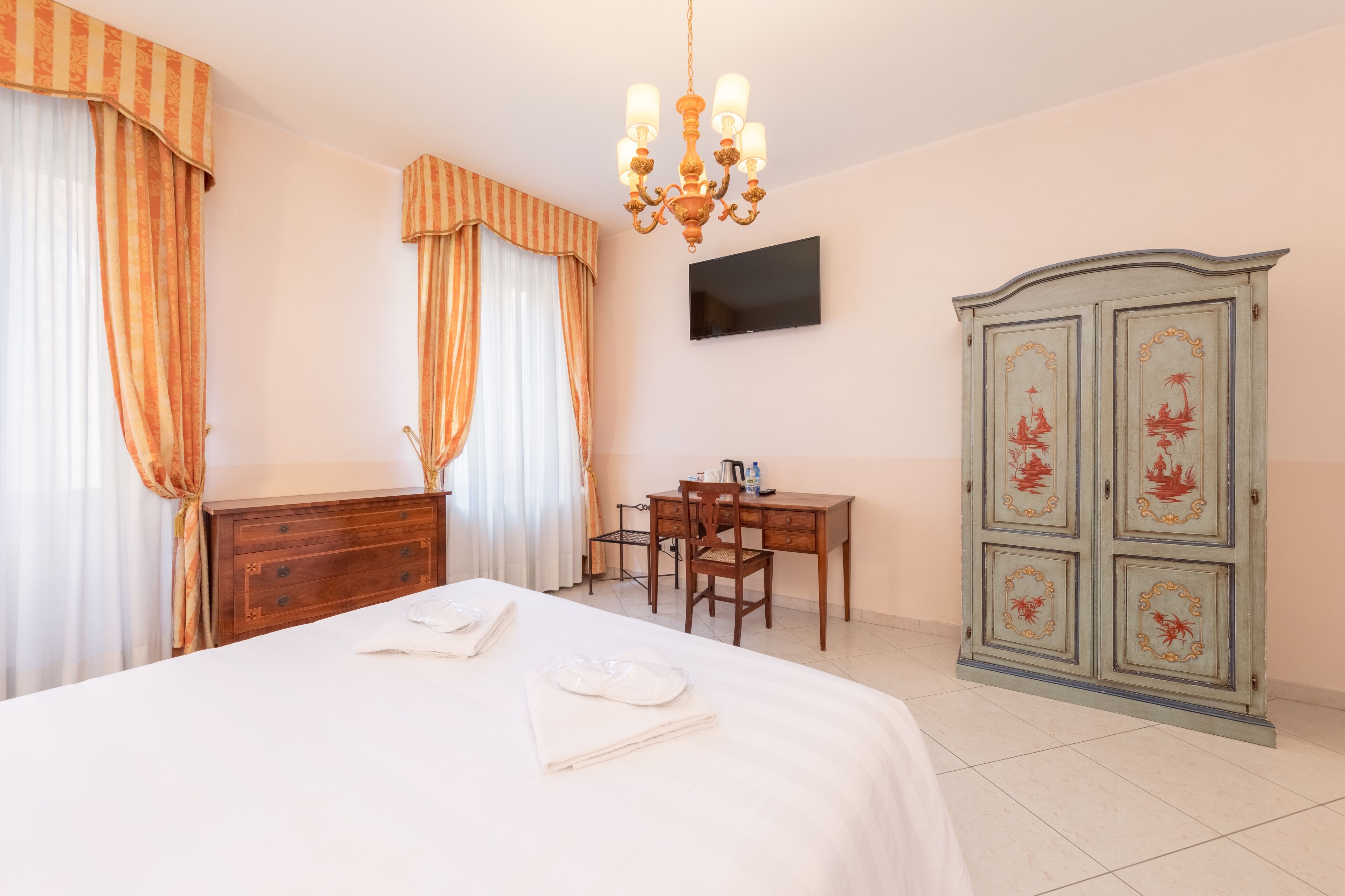 A hotel room with a bed, a desk, a chair, a wardrobe, and a TV on the wall.