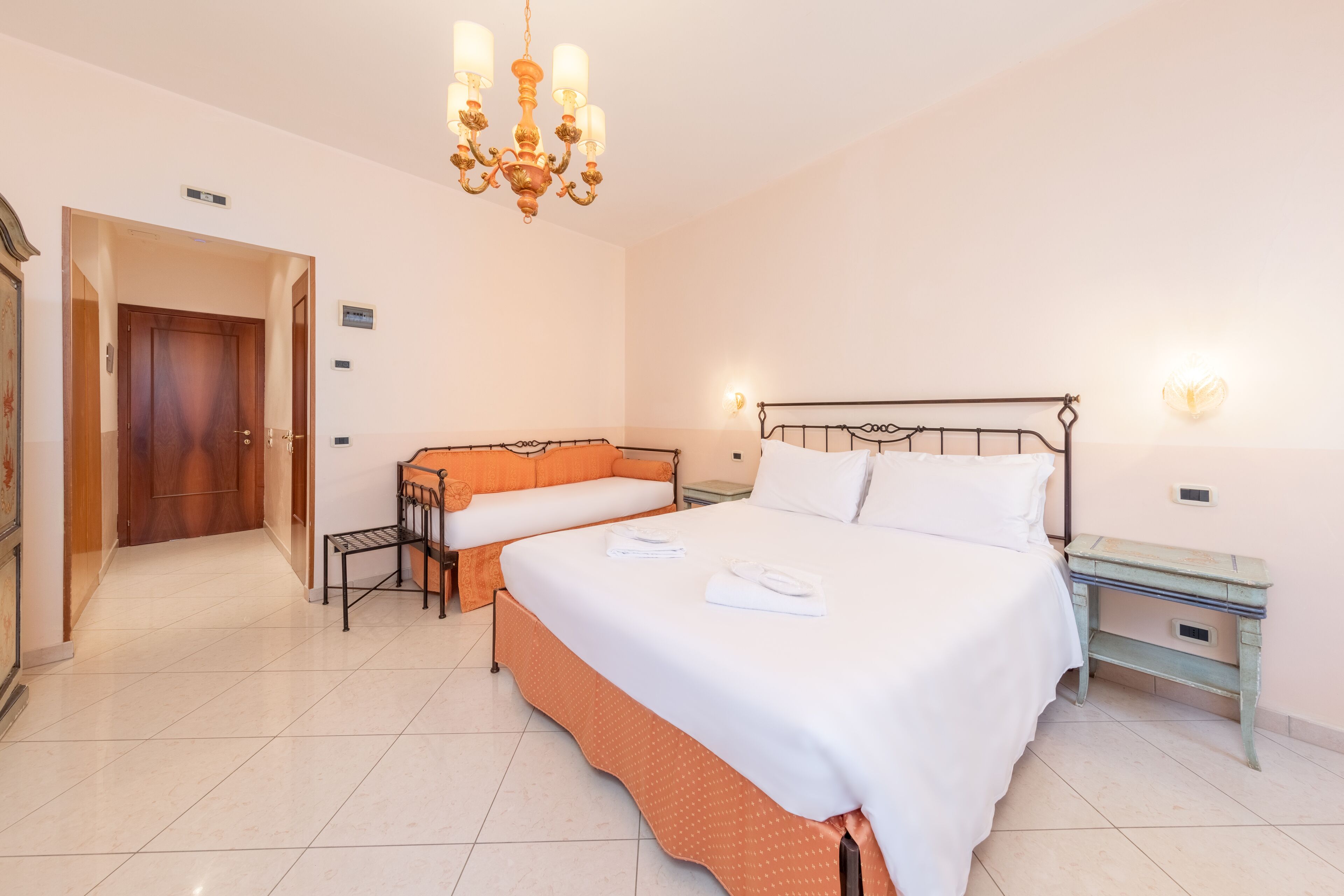 Una camera d'albergo con un letto grande, un divano più piccolo, una scrivania e un lampadario.