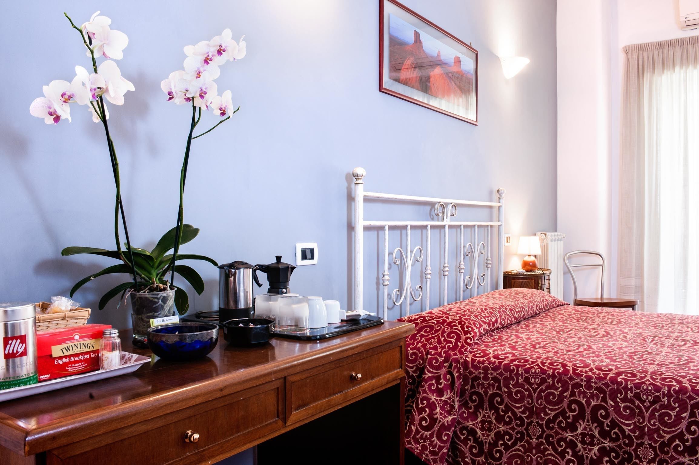 A hotel room with a bed, a wooden dresser, a painting on the wall, and a window with curtains.
