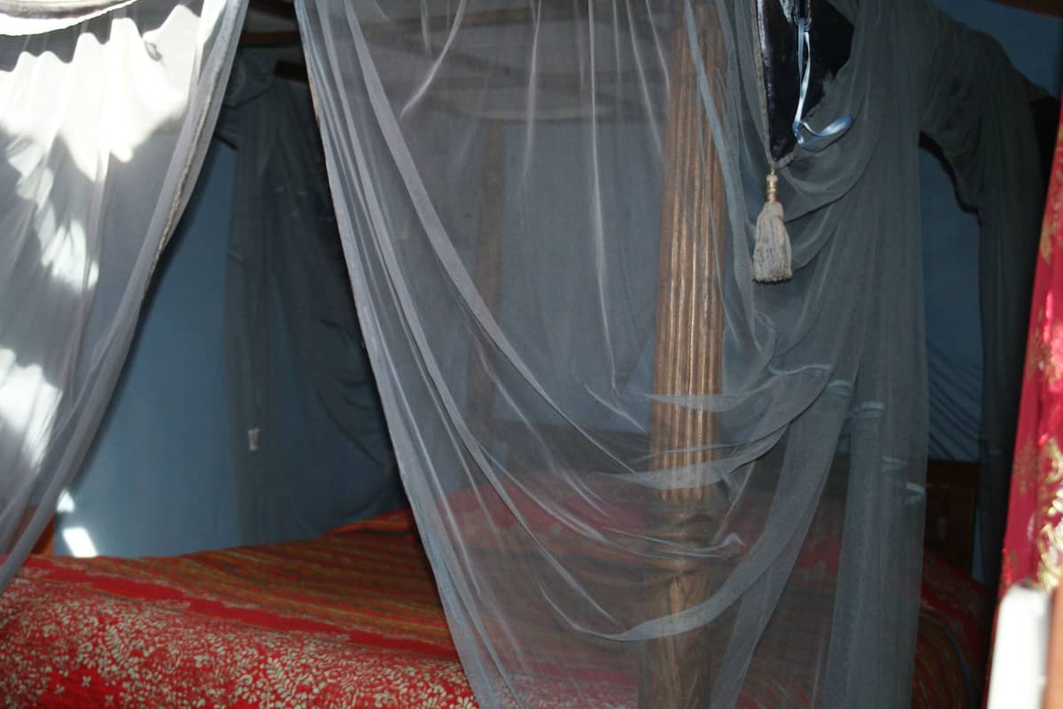 A bed with a red and white patterned bedspread, a wooden headboard, and sheer curtains.