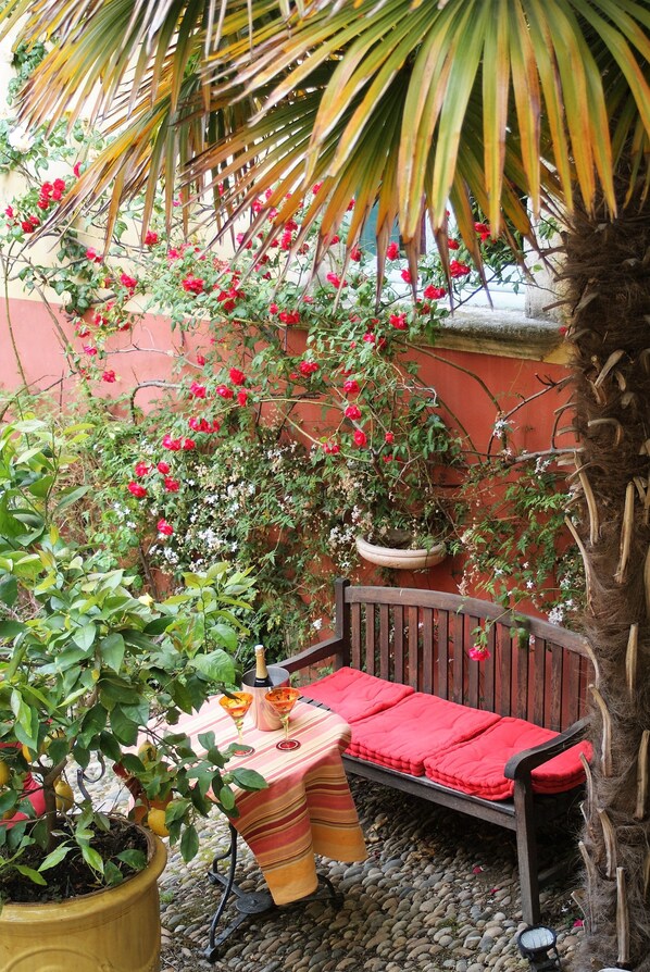 A patio with a wooden bench, a table with a red cloth, and potted plants.