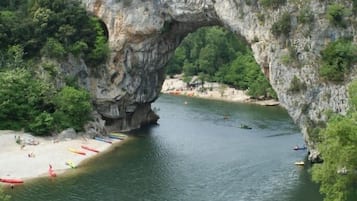 A natural rock arch over a river with a sandy beach and people engaging in water activities.