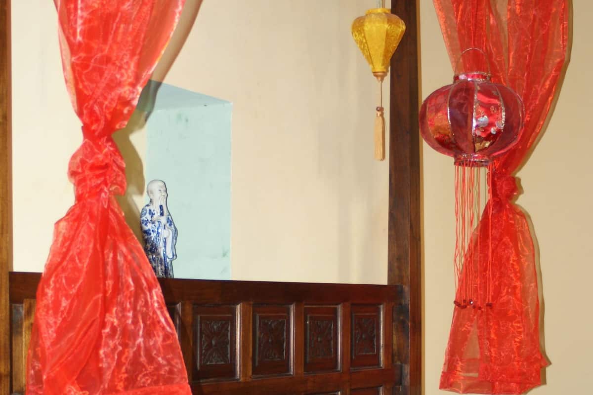 A bed with a colorful quilt, a wooden headboard, and red canopy drapes.
