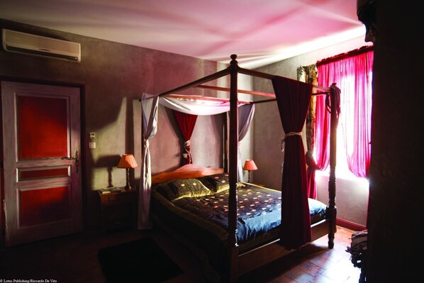 A four-poster canopy bed with a wooden frame and red curtains, a bedside table with a lamp, and a red door. - Hôtel de Digoine - Demeure d'hôtes (Bourg-Saint-Andeol)