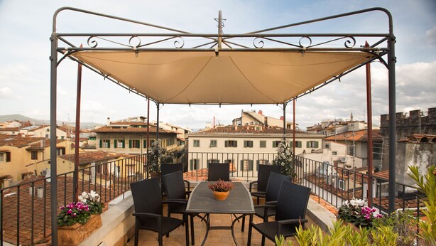 A terrace with a table and chairs, a pergola, and potted plants.