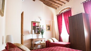 A bedroom with a wooden ceiling, a bed with red bedding, a bedside table, a mirror, and a wardrobe.