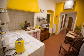 A kitchen with white and yellow tiles, a microwave, a sink, and a dining area with a table and chairs. - Il Bargello (Florence)