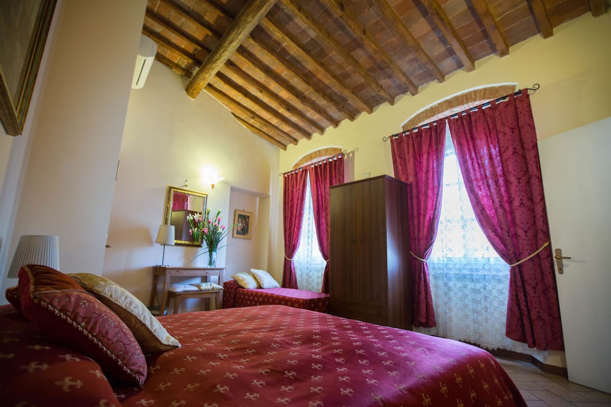 Un dormitorio con techo de madera, una cama con ropa de cama roja, un armario y una ventana con cortinas rojas.