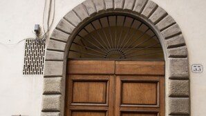 A double wooden door with a stone archway, a metal vent, and a small sign on the wall.
