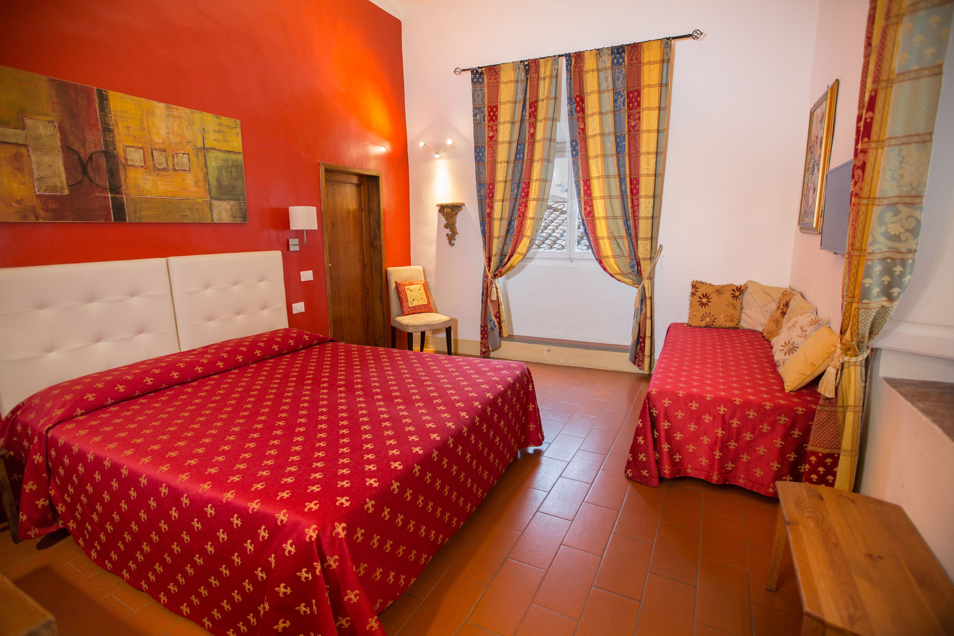 Una habitación de hotel con dos camas, un cuadro grande en la pared, una ventana con cortinas y un banco de madera.