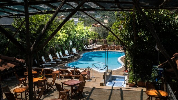 A poolside area with lounge chairs and tables, a pool, and a view of the surrounding landscape. - Villaggio Verde (Sorrento)