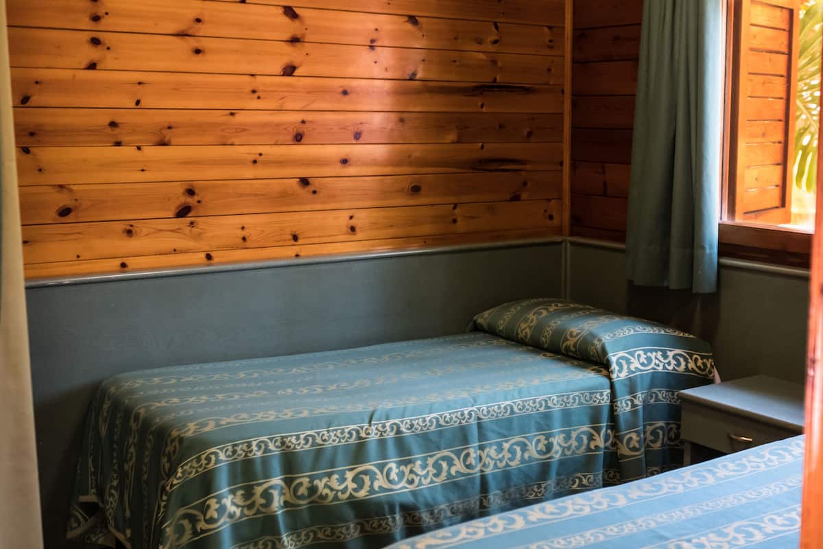 A room with wooden panel walls, a bed with patterned bedding, and a window with a curtain.