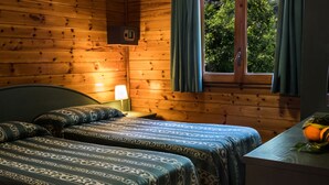 A wooden cabin room with two beds, a nightstand, a lamp, and a window with curtains. - Villaggio Verde (Sorrento)