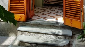 A wooden door with horizontal slats, leading to a room with a bed and a lamp. - Villaggio Verde (Sorrento)