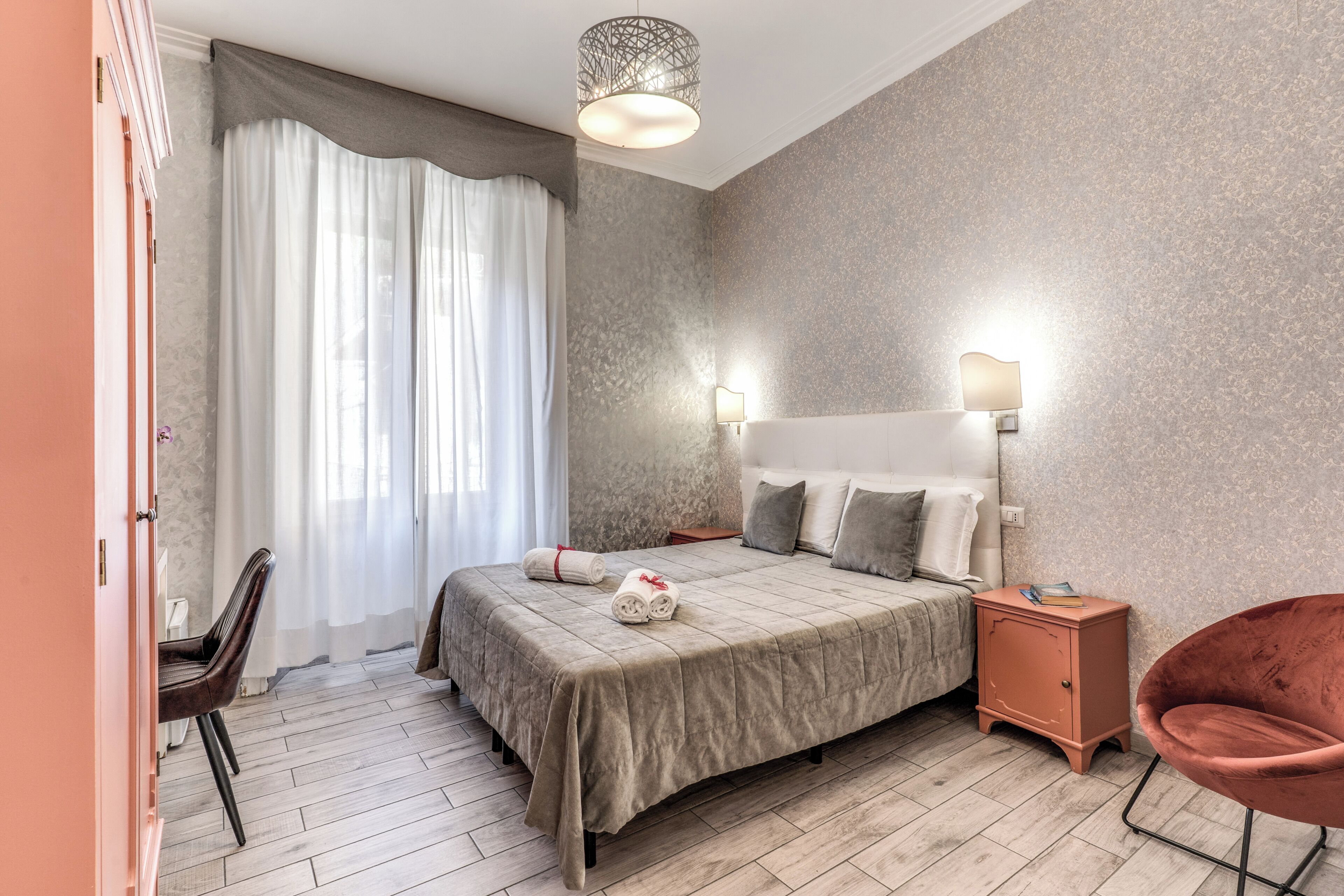 Een slaapkamer met een bed, nachtkastjes, een stoel en een raam met gordijnen.