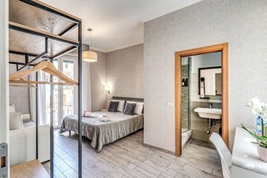 A bedroom with a bed, bedside table, hanging clothes rack, and a bathroom with a sink and mirror. - Marta Inn (Rome)