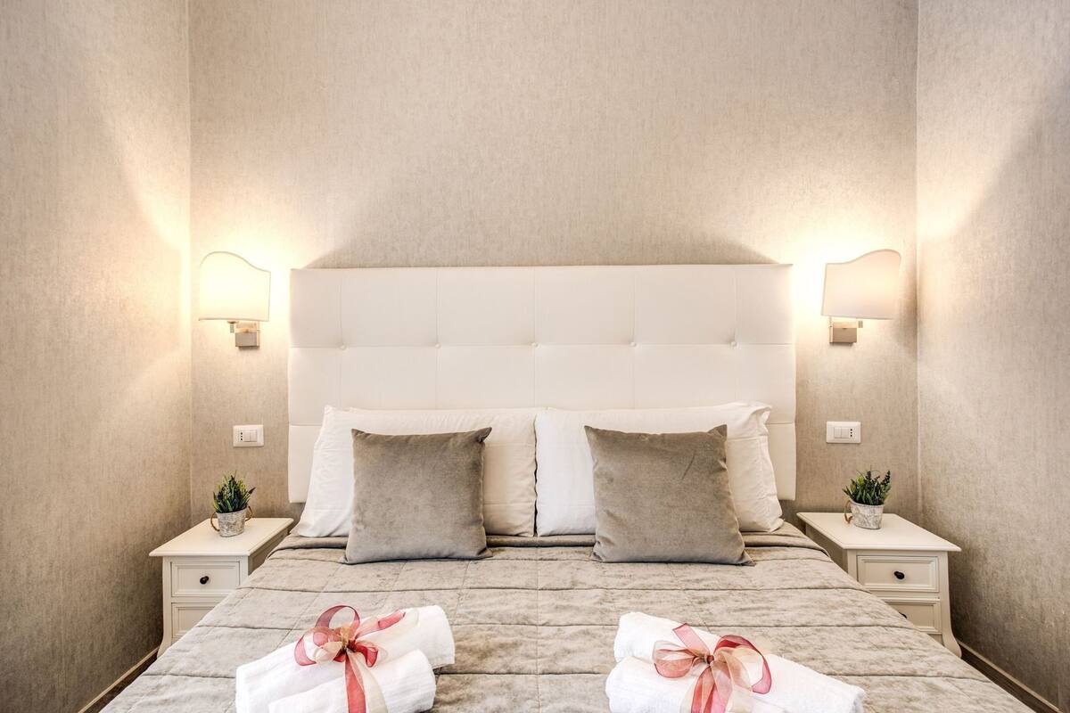 A hotel room with a tufted headboard, two bedside tables with lamps, and a bed with two pillows.
