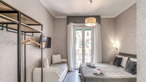 A hotel room with a bed, a sofa, a TV, a hanging rack, and a window with curtains. - Marta Inn (Rome)