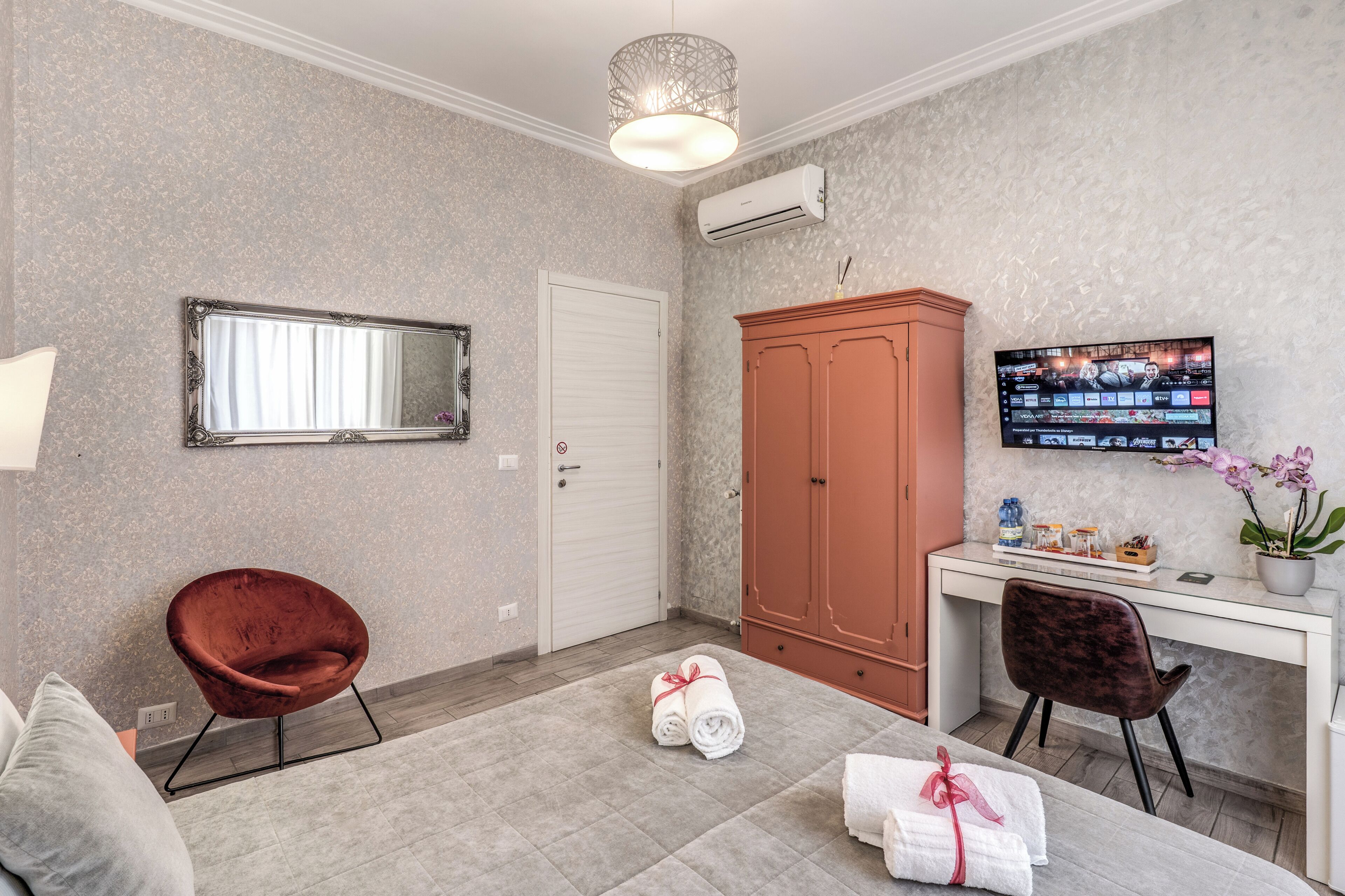Una habitación moderna con un espejo grande, armario, televisor y un escritorio con silla.