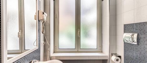 A bathroom with a large window, a bathtub, a sink, and a toilet.